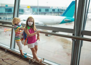 Kids at airport in face mask. Children look at airplane after coronavirus outbreak. Safe travel and flying with child in virus pandemic. Family at departure gate. Vacation after covid-19 lockdown.